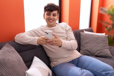 Non binary man using smartphone sitting on sofa at home