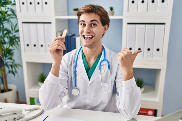 Young Doctor Man Holding Band Aid Pointing Thumb Side Smiling — Stock Photo, Image