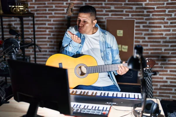 Joven Hispano Tocando Guitarra Clásica Estudio Música Mirando Cámara Soplando —  Fotos de Stock