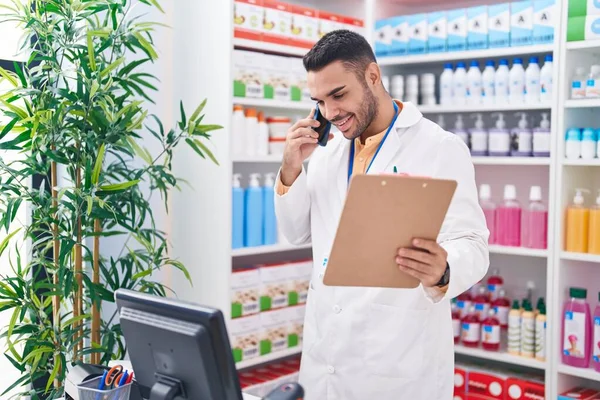 Young Hispanic Man Pharmacist Talking Smartphone Reading Document Pharmacy — Stockfoto