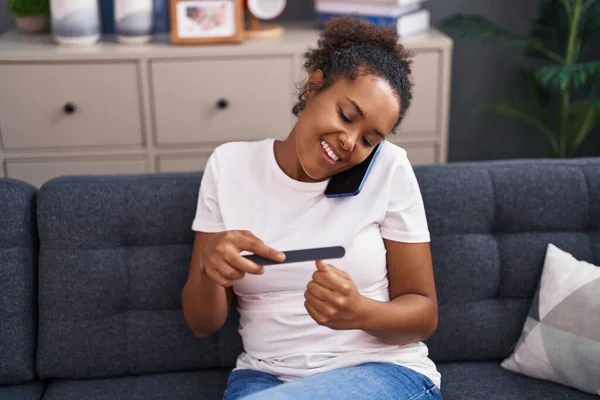 アフリカ系アメリカ人女性が自宅でマニキュアをしているスマートフォンで話しています — ストック写真