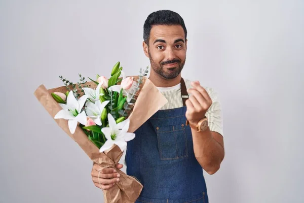 Hispanic man with beard working as florist doing money gesture with hands, asking for salary payment, millionaire business