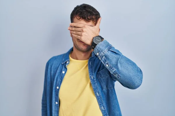 Young Hispanic Man Standing Blue Background Covering Eyes Hand Looking — Fotografia de Stock