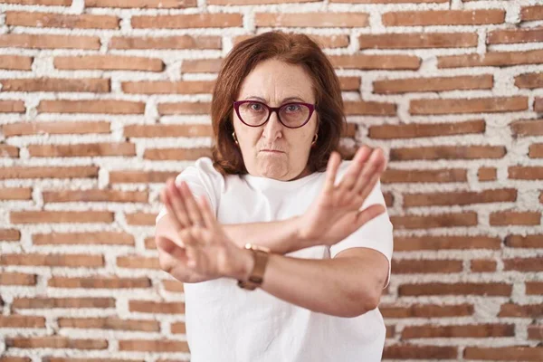 戴眼镜的老妇人站在砖墙上 拒绝表情 胳膊和手掌交叉 做着负面手势 生气的脸 — 图库照片