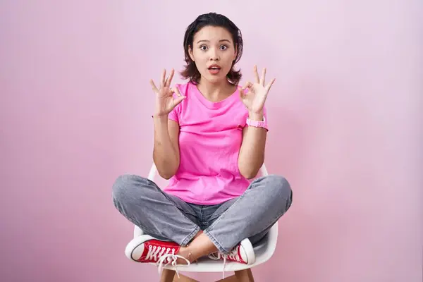 Spaanse Jonge Vrouw Zit Stoel Roze Achtergrond Kijken Verrast Geschokt — Stockfoto
