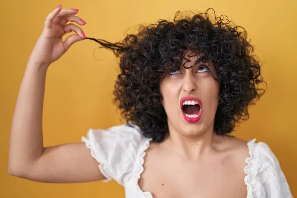stock image Young brunette woman with curly hair holding curl angry and mad screaming frustrated and furious, shouting with anger looking up. 