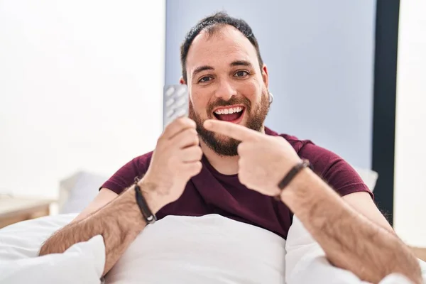 Size Hispanic Man Beard Bed Holding Pills Smiling Happy Pointing — Stock Photo, Image