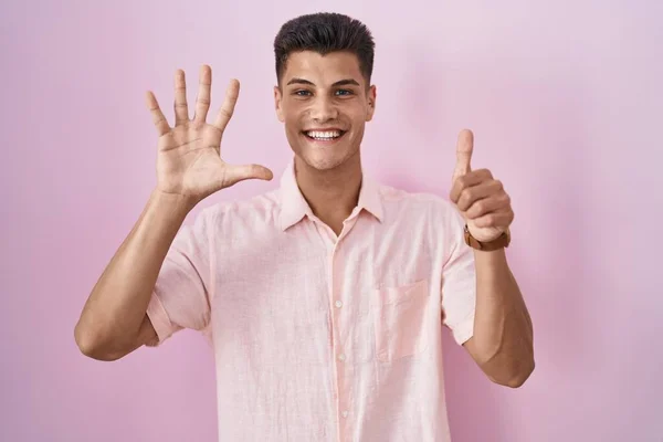 年轻的他的惊慌失措的男人站在粉色的背景上 带着自信和快乐的微笑 用六号手指指指着 — 图库照片