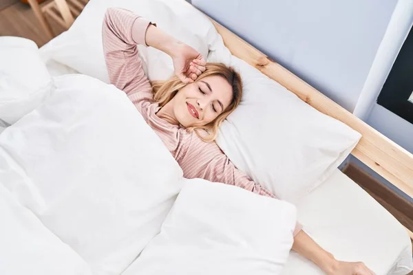 stock image Young blonde woman waking up stretching arms at bedroom