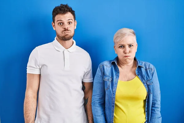 年轻的巴西母亲和儿子站在蓝色的背景上 脸上带着滑稽的表情 气喘吁吁的嘴 疯狂的表情 — 图库照片