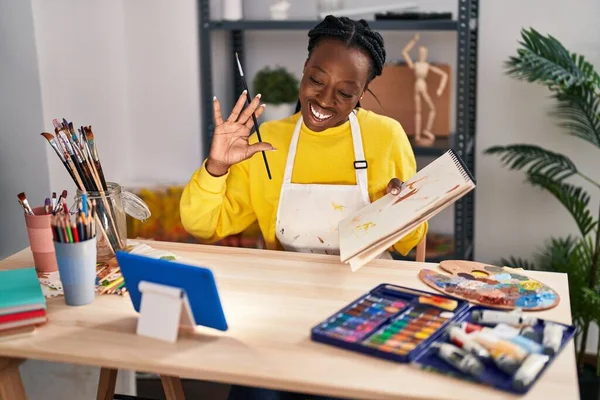 アフリカ系アメリカ人女性アーティストノートブックにビデオ通話を持つアートスタジオで描く — ストック写真