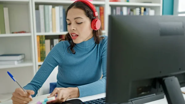 年轻美丽的惊慌失措的女学生带着耳机在大学教室里用电脑记笔记 — 图库照片
