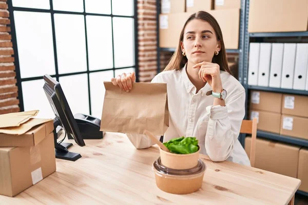中小企業で働く若い白人女性が食べ物を奪う深刻な顔あごに手で質問について考える 混乱のアイデアについて思慮深い — ストック写真