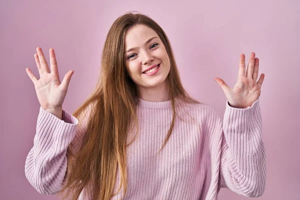 年轻的高加索女人站在粉红的背景上 带着自信和快乐的微笑 指指点着十号 — 图库照片