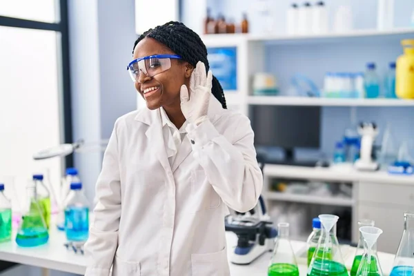 科学研究所で働くアフリカ系アメリカ人女性は 耳を傾け 噂やゴシップに耳を傾けながら笑顔で働いています 聴覚障害の概念 — ストック写真