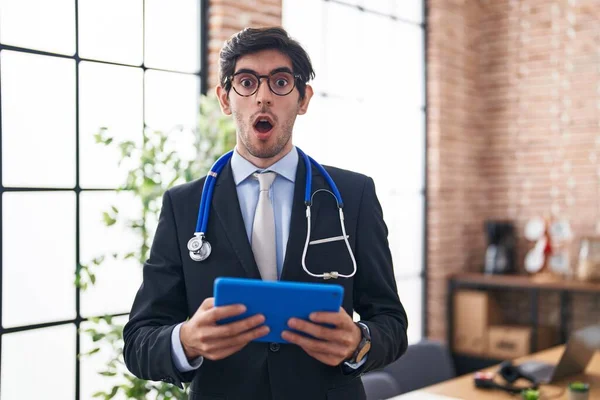 Młody Hiszpan Noszący Biurze Stetoskop Doktorski Szokującej Twarzy Wyglądający Sceptycznie — Zdjęcie stockowe