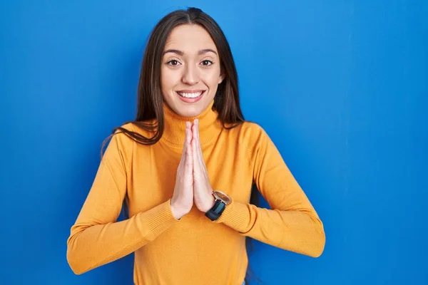Jonge Brunette Vrouw Staande Blauwe Achtergrond Bidden Met Handen Samen — Stockfoto