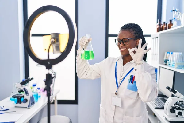 科学研究所で働いているアフリカの女性は 指でOkサインを行うスマートフォンでチュートリアルを行います 笑顔に優しいジェスチャー優れたシンボル — ストック写真