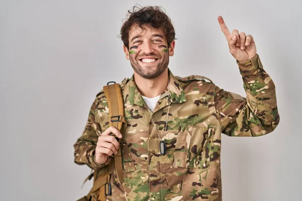 Spanskættede Unge Mann Med Kamuflasjeuniform Smiler Forbløffet Overrasket Peker Opp – stockfoto