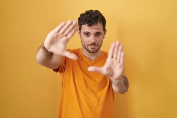 Young Hispanic Man Standing Yellow Background Doing Frame Using Hands — 스톡 사진