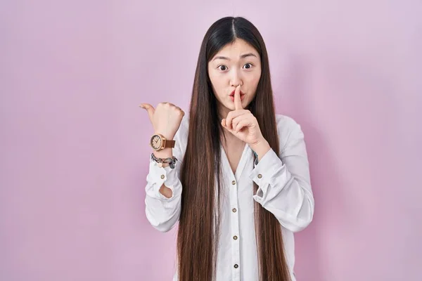 中国的年轻女子站在粉色的背景上 要求保持安静 手指放在嘴唇上 手放在侧面 沉默和秘密概念 — 图库照片