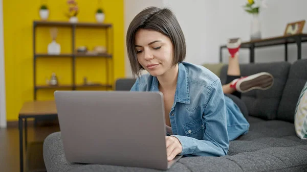 使用笔记本电脑的年轻高加索女人躺在家里的沙发上 — 图库照片