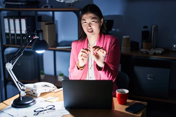 Chinese young woman working at the office at night disgusted expression, displeased and fearful doing disgust face because aversion reaction. with hands raised