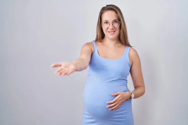 Молодая Беременная Женщина Стоящая Белом Фоне Весело Улыбаясь Протягивая Руку — стоковое фото