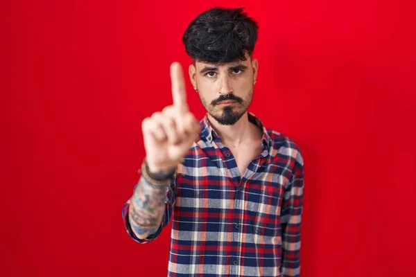 Kırmızı Arka Planda Sakallı Genç Spanyol Bir Adam Parmağını Kaldırmış — Stok fotoğraf