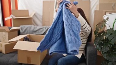 Young beautiful hispanic woman unpacking cardboard box at new home