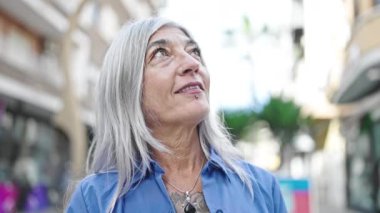 Orta yaşlı, kır saçlı, gülümseyen, kendine güvenen bir kadın.