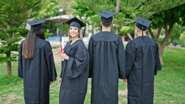 Bir grup öğrenci üniversite kampüsünde el ele selamlaşarak diploma alarak mezun oldular.