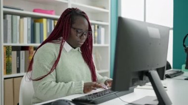 Saçları örülmüş Afrikalı bir kadın üniversite kütüphanesinde bilgisayar kullanıyor.