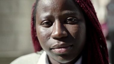 Örgülü saçlı Afrikalı kadın sokakta ciddi bir ifadeyle ayakta duruyor.