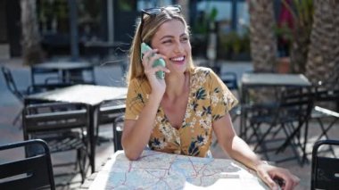 Genç sarışın kadın turist akıllı telefondan konuşuyor. Şehir haritasını kahve dükkanının terasında görüyor.