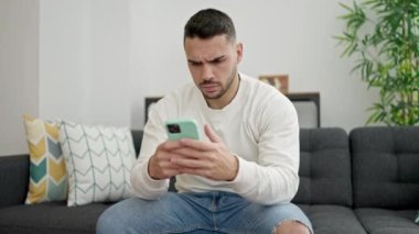 Genç İspanyol adam evde akıllı telefon kullanarak kanepede otururken strese girdi.