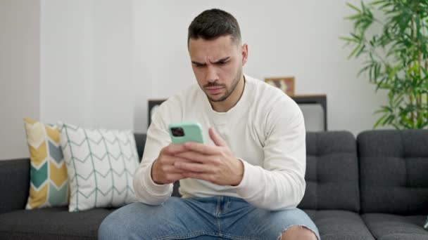 Young Hispanic Man Stressed Sitting Sofa Using Smartphone Home — Stock Video