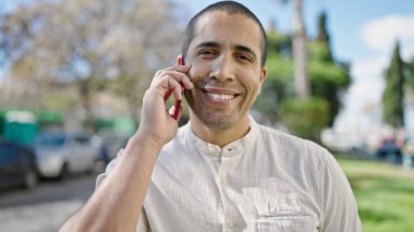Genç İspanyol adam parkta telefonla konuşuyor.
