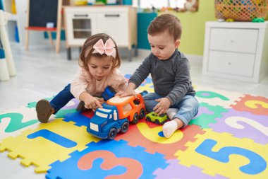 Sevimli çocuk ve kız arabalarla oynuyorlar. Anaokulunda yerde oturuyorlar.