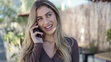 Young blonde woman smiling confident talking on the smartphone at coffee shop terrace