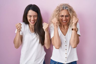 Pembe arka planda bir arada duran anne ve kız kolları havada ve gözleri kapalı zaferi kutluyorlar. Kazanan konsept. 