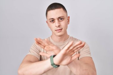 İzole edilmiş arka plan reddedilmesinin başında duran genç adam kollarını ve avuçlarını çaprazlayarak negatif işaret veriyor, kızgın yüz ifadesi. 