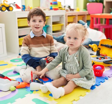 Süpermarket oyunu oynayan sevimli bir çocuk ve kız anaokulunun zemininde oturuyorlar.