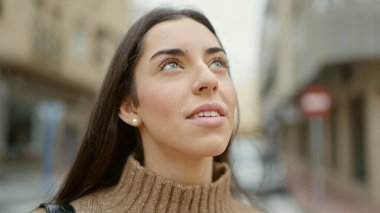 Young beautiful hispanic woman smiling confident looking to the sky at street
