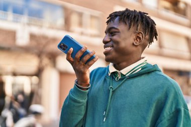 Afro-Amerikalı adam gülümsüyor. Kendine güveniyor. Akıllı telefondan konuşuyor.