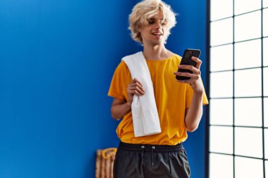 Spor merkezinde akıllı telefon kullanan kendine güvenen genç sarışın adam.