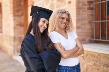 Two women mother and graduated daughter standing with arms crossed gesture at campus university