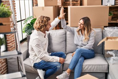 Man and woman couple high five with hands raised up sitting on sofa at new home