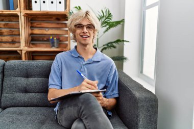 Genç sarışın adam psikolog psikoloji kliniğindeki belgeye yazı yazıyor.