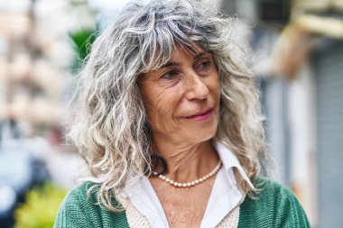 Orta yaşlı bir kadın sokakta kendine güvenerek gülümsüyor.